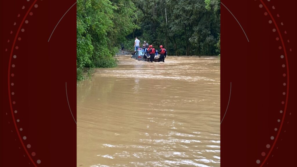 Carro parcialmente submerso em estrada rural alagada no Paraná.