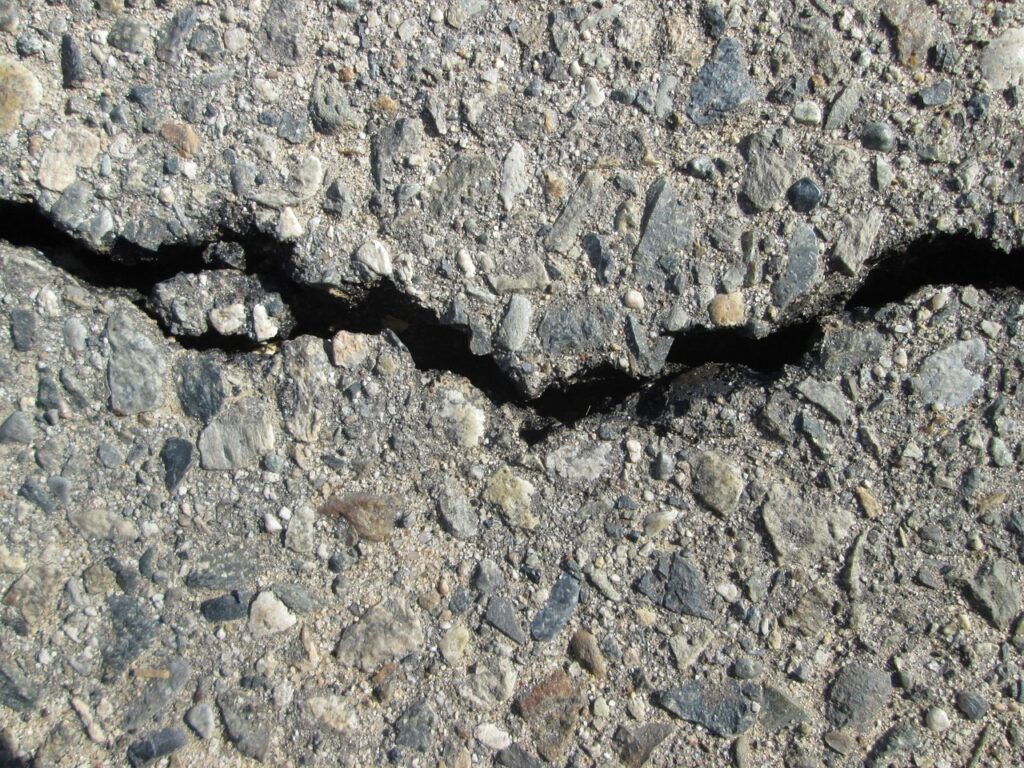 Rachadura profunda em pavimento de asfalto com pedras aparentes, sinal de desgaste na pista