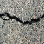 Rachadura profunda em pavimento de asfalto com pedras aparentes, sinal de desgaste na pista