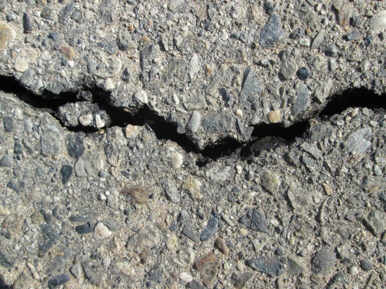 Rachadura profunda em pavimento de asfalto com pedras aparentes, sinal de desgaste na pista