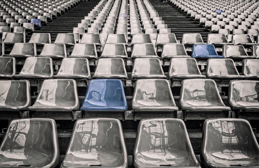 Arquibancada vazia de estádio, com fileiras de assentos cinza e um único assento azul em destaque