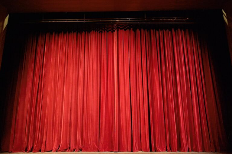 Cortina vermelha de veludo fechada em um palco de teatro vazio, com iluminação suave