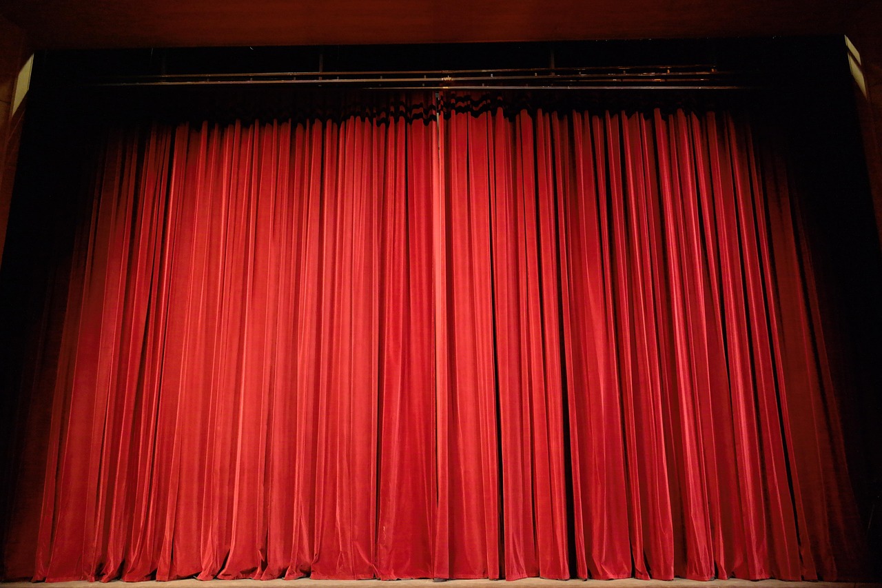 Cortina vermelha de veludo fechada em um palco de teatro vazio, com iluminação suave