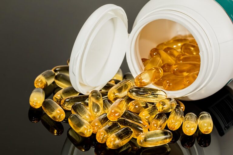Cápsulas de gel amarelas saindo de um frasco branco aberto sobre superfície escura e reflexiva